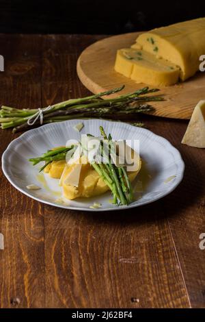 Gerollter Maisbrei mit Spargel und Käseflocken auf weißem Teller und dunklem Holzhintergrund Stockfoto