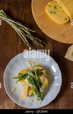 Gerollter Maisbrei mit Spargel und Käseflocken auf weißem Teller und dunklem Holzhintergrund Stockfoto