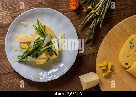 Gerollter Maisbrei mit Spargel und Käseflocken auf weißem Teller und dunklem Holzhintergrund Stockfoto