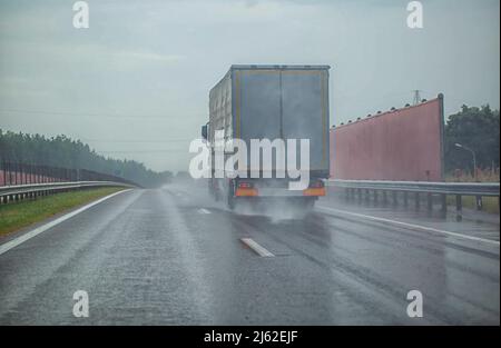 Sattelschlepper, der mit anderen Autos bei starkem Regen im Sommer auf der Autobahn fährt, nasse Straße. Verkehr auf der Straße, Distanz halten, Hintergrund Stockfoto