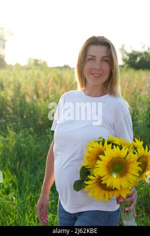 Schwanger im Sommer. Glücklich schwanger junge Frau mit Blumenstrauß draußen genießen die Natur. Stockfoto