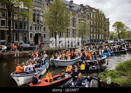 AMSTERDAM, Niederlande, 2022-04-27 - Nachtschwärmer auf dem Wasser, es ist sehr beschäftigt auf den Kanälen in der Hauptstadt. Nach zwei Jahren, in denen der King's Day aufgrund der Corona-Pandemie in kleinem Umfang gefeiert werden musste, wird die Party auch in diesem Jahr wieder im großen Stil gefeiert. ANP RAMON VAN FLYMEN niederlande Out - belgien Out Stockfoto