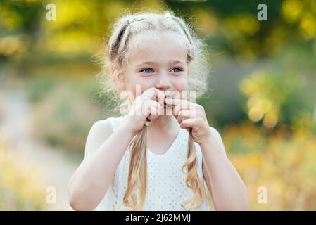 Funny Girl holding Haar Zöpfe. Kleine süße Mädchen mit langen blonden Haaren outdoor. Kid Emotionen zum Ausdruck zu bringen. April Stockfoto