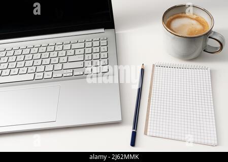 Laptop-Computer und Notizblock auf weißem Schreibtisch mit einer Tasse Kaffee Stockfoto