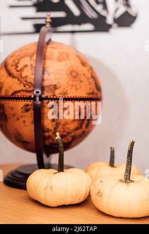 Auf einem Holztisch liegen drei kleine Kürbisse in der Nähe des Globus Stockfoto