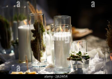 Hochzeitsfeier Bankett im Freien im Wald. Esstisch im Boho-Stil mit Kerzen, weißem Tuch, Blumen, serviert mit Tellern, Geschirr dekoriert Stockfoto