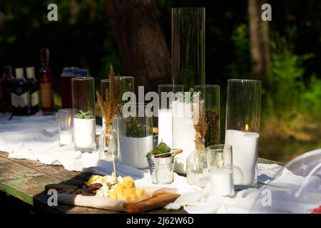Hochzeitsfeier im Freien im Pinienwald. Esstische im Boho-Stil mit Kerzen in Glasvasen, weißen Stoffen und sukkkulenten Blumen dekoriert. Eco Stockfoto