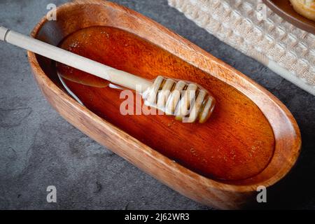 Honig in Holzschale mit Honigtaue auf grauem Hintergrund Stockfoto