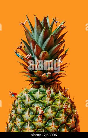 Einige Miniaturmenschen, die Badeanzug tragen, in verschiedenen Aktionen, auf einer Ananas, vor einem orangen Hintergrund Stockfoto