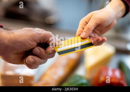 Nicht erkennbarer männlicher Kunde, der die Kreditkarte an den Kassierer übergibt Stockfoto