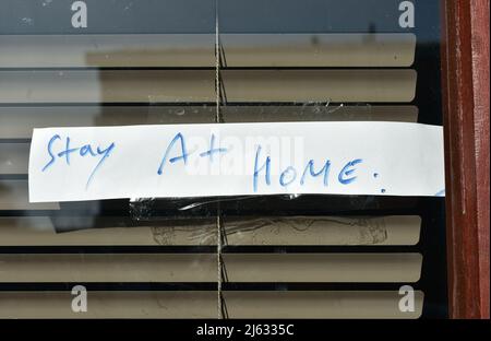 Richard und Lisa's Convenience Store-Schaufenster mit Einem Schild mit der Aufschrift „zu Hause bleiben“ auch Schutz vor Covid-19 Stockfoto