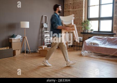 Horizontale Seitenansicht des jungen kaukasischen Mannes, der in eine neue Wohnung umzieht und Stühle in die Wohnung bringt Stockfoto