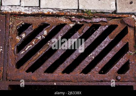 Eine alte rostige Schachtbohrung zur Aufnahme von Regenwasser oder geschmolzenem Schnee. Vor dem Hintergrund von grauen Pflasterplatten. Blick von oben Stockfoto
