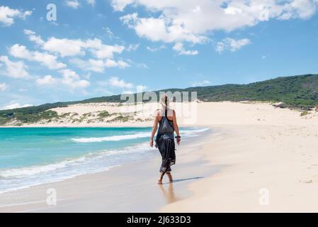 Kaukasische blonde Frau, die am Strand von Valdevaqueros in Tarifa Spanien entlang läuft, mit einer großen Düne im Hintergrund Stockfoto