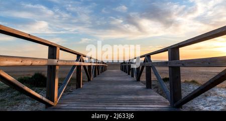 Panoramablick auf einen Holzsteg, der bei Sonnenuntergang zum Strand führt, mit einem wunderschönen bewölkten Himmel Stockfoto