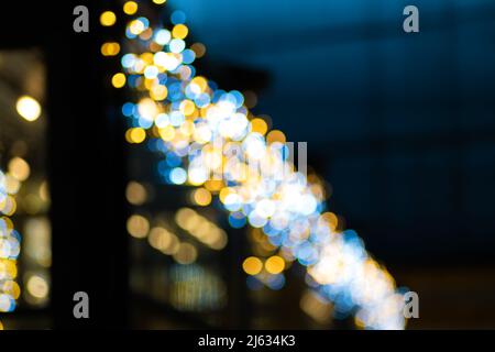 Verschwommener Hintergrund des Bokeh der gelb-blauen Weihnachtslichter auf der Straße in der Nacht, kopieren Sie den Raum. Verschwommene Lichter der Nachtstadt, Bokeh Stockfoto