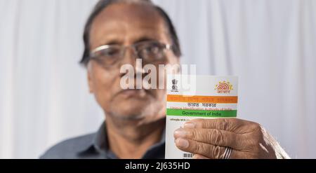 Birbhum, Westbengalen / Indien - 15. März 2022: Selektiver Fokus auf die Aadhaar-Karte, die von einem alten indischen Mann mit lächelndem Gesicht in der Hand gehalten wird Stockfoto