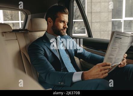 Fokussierter bärtiger Geschäftsmann, der in der Geschäftsliteratur im Auto nachschaut Stockfoto