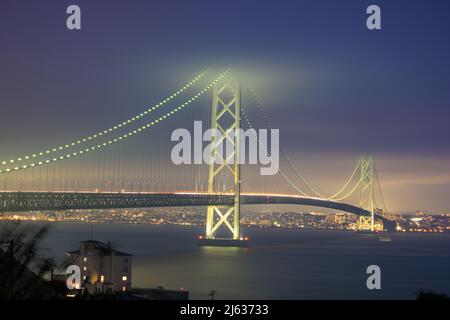 Der Verkehr bewegt sich entlang der Hängebrücke, die in der bewölkten Nacht beleuchtet wird Stockfoto