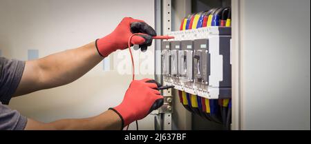 Elektroingenieure überprüfen elektrische Steuergeräte mit einem Multimeter. Stockfoto