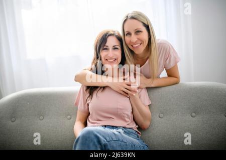 Zwei lächelnde beste Mädchen Freunde blond und brünette sitzen auf dem Sofa Stockfoto