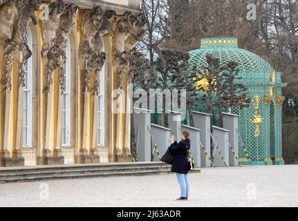 Potsdam, Deutschland. 17. März 2022. Eine junge Frau macht ein Foto vor dem Schloss Sanssouci. Die Statuen im Park sind wegen der kalten Jahreszeit durch Holzhauben geschützt. Quelle: Soeren Stache/dpa-Zentralbild/ZB/dpa/Alamy Live News Stockfoto