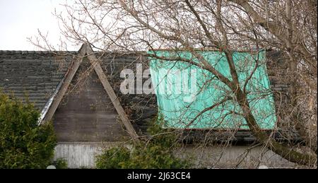 Wohndach, das dringend repariert oder ersetzt werden muss, mit abblätternden Schindeln und Tarp Stockfoto