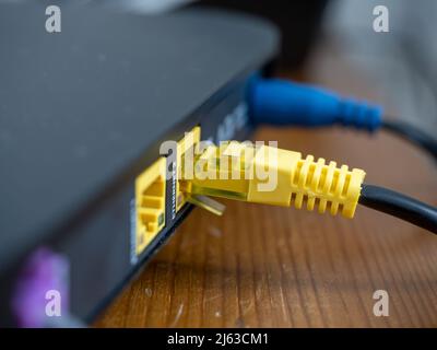 Nahaufnahme einer gelben Ethernet-Verbindung zu einem drahtlosen Breitband-Router für Hochgeschwindigkeitsdatenübertragungen Stockfoto