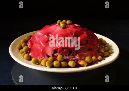 Heringsalat unter einem Pelzmantel auf einem weißen Teller auf dem Tisch. Essen auf schwarzem Hintergrund Stockfoto