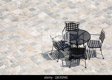 Blick von oben auf eine komfortable Terrasse mit schmiedeeisernem Tisch und Stühlen auf einer gepflasterten Terrasse. Stockfoto