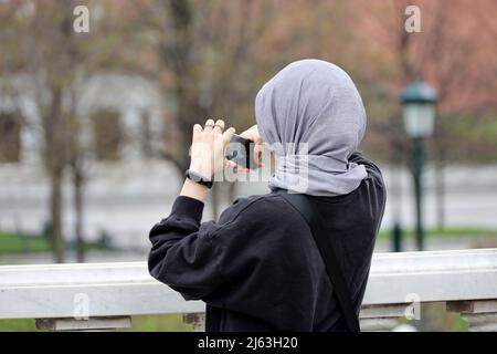 Muslimische Frau, die Fotos auf der Smartphone-Kamera auf der Straße der Stadt. Mädchen in Hijab im Frühling Park Stockfoto