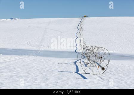 Ein Radlinen-Sprinkler auf einem Feld, im Winter mit Schnee auf dem Boden. Stockfoto