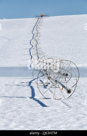 Ein Radlinen-Sprinkler auf einem Feld, im Winter mit Schnee auf dem Boden. Stockfoto