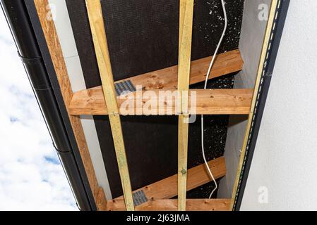 Gerüst mit drei Reihen von Holzlatten zur Befestigung der PVC-Soffit, sichtbare Kabel für die Beleuchtung. Stockfoto