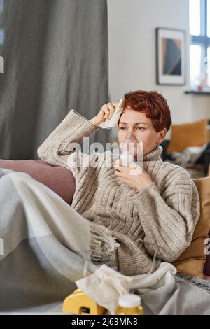 Vertikale mittlere Aufnahme von reifen kaukasischen Frau mit kurzen roten Haaren mit Coronavirus Entspannung zu Hause mit Vernebler Stockfoto