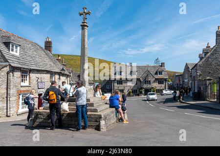 Corfe Castle Dorfzentrum mit Menschen rund um das Kriegs-Gedenkkreuz, Dorset, England, Großbritannien, an einem sonnigen Apriltag Stockfoto