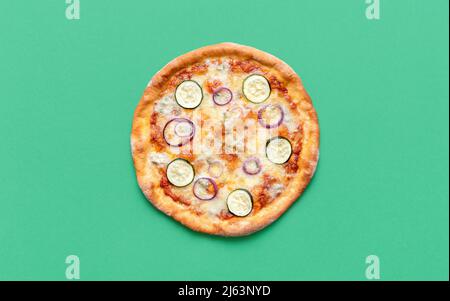 Blick von oben mit einer ganzen vegetarischen Pizza auf einem grünen Tisch. Köstliche hausgemachte Pizza mit roten Zwiebeln, Gorgonzola, Mozzarella und Zucchini. Stockfoto