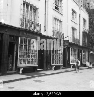 1960s, historisch, Woburn Walk, Bloomsbury, London, England, Großbritannien. Auf dem Bild sind die Woburn Buchhandlung und rechts Sutherlands Antiquitäten zu sehen. Der Name der Fußgängerzone ist von der Woburn Abbey abgeleitet, dem englischen Landsitz der Herzöge von Bedford, der das Gebiet besaß und entwickelte. 1822 von Thomas Cubitt entworfen, war sie Londons erste zweckmäßig gebaute Fußgängerzone mit Einkaufsstraßen. Die Schaufensterfronten haben ein unverwechselbares Aussehen, die Fenster bestehen aus kleinen, einzelnen Glasscheiben und sind mit einer Dickenser-Bogenfront versehen. Stockfoto