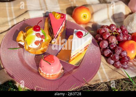 Zusammensetzung auf einer Tagesdecke aus Kuchen, Trauben und Pfirsichen Stockfoto