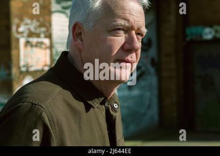 Nahaufnahme von Kopf und Schultern eines Mannes mittleren Alters in einer Stadtstraße. Er hat einen ernsten Ausdruck und blickt aus dem Rahmen zur Seite. Stockfoto