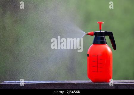 Manuelles Wassersprühen. Der orangefarbene Tank sprüht Wassertropfen mit Druck Stockfoto