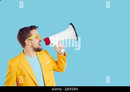 Junger expressiver Mann mit Megaphon kündigt Rabatte und Verkäufe auf hellblauem Hintergrund an. Stockfoto