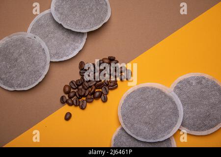 Draufsicht auf Kaffeepads und Kaffeebohnen auf orangefarbenem und braunem Karton im 45-Grad-Winkel als Beispiel für verschiedene Kaffeerohprodukte. Flach Lay CO Stockfoto