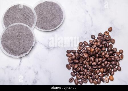 Draufsicht auf Kaffeepads und Kaffeebohnen auf einer Marmoroberfläche als Beispiel für verschiedene Kaffeerohprodukte. Flache Lay-Komposition Stockfoto