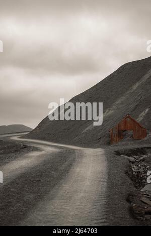 Verderbtes Welleisen-Haus, halb begraben in einem großen Schieferhaufen in der Nähe der Hollister Schiefer Mine im Lake District National Park, Cumbria, England, Großbritannien Stockfoto