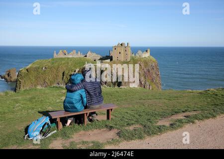 Dunnottar Castle, Stonehaven, Aberdeenshire, Schottland, Ein Paar kuschelt sich vor dem Schloss, Einer zerstörten mittelalterlichen Festung auf einer felsigen Landzunge an der Nordostküste Schottlands, etwa 2 Meilen südlich von Stonehaven. Die erhaltenen Gebäude stammen größtenteils aus dem 15.. Und 16.. Jahrhundert, aber es wird angenommen, dass die Stätte im frühen Mittelalter befestigt wurde. Auf einem 160 Meter hohen Felsen gelegen und auf drei Seiten von der Nordsee umgeben, waren diese dramatischen und eindrucksvollen Ruinen auf einer Klippe einst eine uneinnehmbare Festung des Earls Marischal, einst eine der mächtigsten Familien Schottlands. Stockfoto