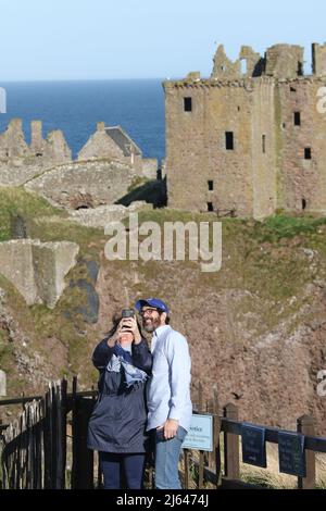Dunnottar Castle, Stonehaven, Aberdeenshire, Schottland, Großbritannien. Paar machen ein Selfie mit Schloss. Eine zerstörte mittelalterliche Festung auf einer felsigen Landzunge an der Nordostküste Schottlands, etwa 2 Meilen südlich von Stonehaven. Die erhaltenen Gebäude stammen größtenteils aus dem 15.. Und 16.. Jahrhundert, aber es wird angenommen, dass die Stätte im frühen Mittelalter befestigt wurde. Auf einem 160 Meter hohen Felsen gelegen und auf drei Seiten von der Nordsee umgeben, waren diese dramatischen und eindrucksvollen Ruinen auf einer Klippe einst eine uneinnehmbare Festung des Earls Marischal, einst eine der mächtigsten Familien Schottlands. Stockfoto