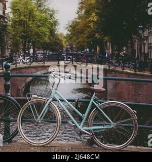 Vintage Teal Fahrrad geparkt auf einer Brücke am Kanal in Amsterdam, Niederlande Stockfoto