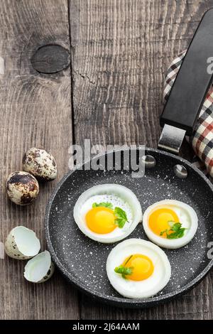 Gebratene Wachteleier in Zwiebelring in Bratpfanne auf Holztisch Stockfoto