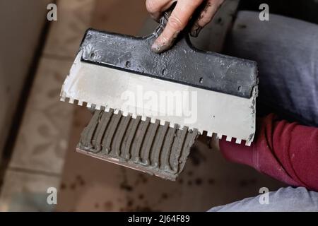 Ein Mann trägt Fliesenkleber mit einer Kelle auf eine Fliese auf. Fliesen an die Wand legen. Stockfoto